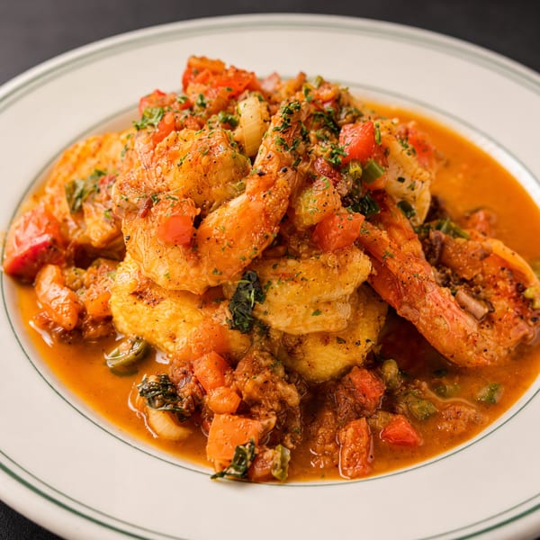 Shrimp and grits with a rich tomato-based sauce, garnished with fresh herbs on a white plate.