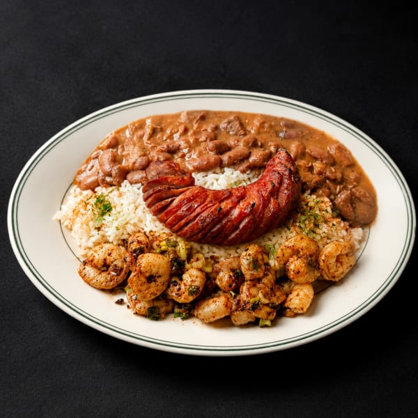 Cajun platter with red beans and rice, grilled sausage, and seasoned shrimp on a white plate.