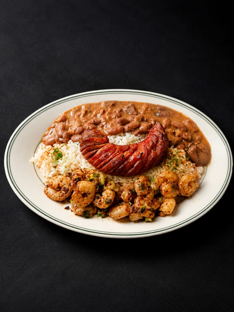 Cajun platter with red beans and rice, grilled sausage, and seasoned shrimp on a white plate.