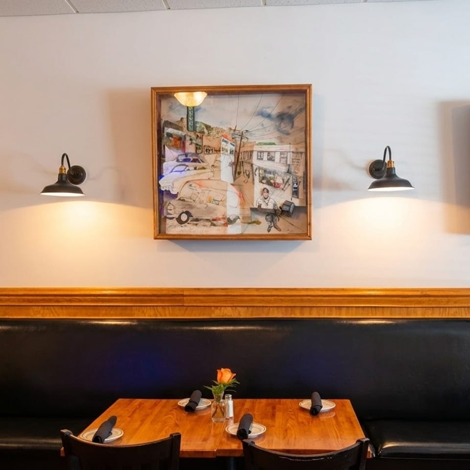 Restaurant interior with black booth seating, wooden tables, and framed artwork on a white wall.