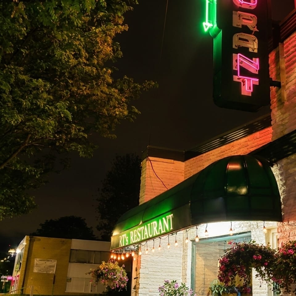 Exterior of RT's Restaurant at night, with green awnings, string lights, and hanging flower baskets.