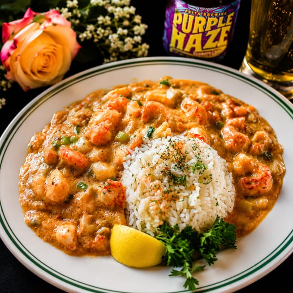 Crawfish étouffée with rice, lemon, and parsley, with a beer and rose in the background.